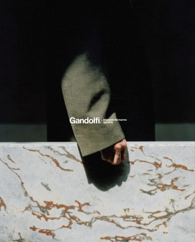 Visual Gandolfi con logo bianco e una persona in giacca verde accanto a una lastra di marmo venato.